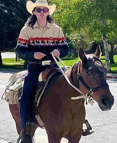 Person in a cowboy hat riding a brown horse outdoors on a sunny path