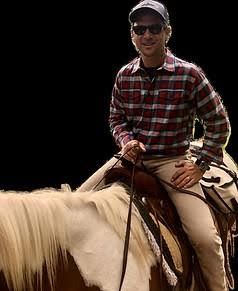 Person in plaid shirt and sunglasses riding a white horse outdoors