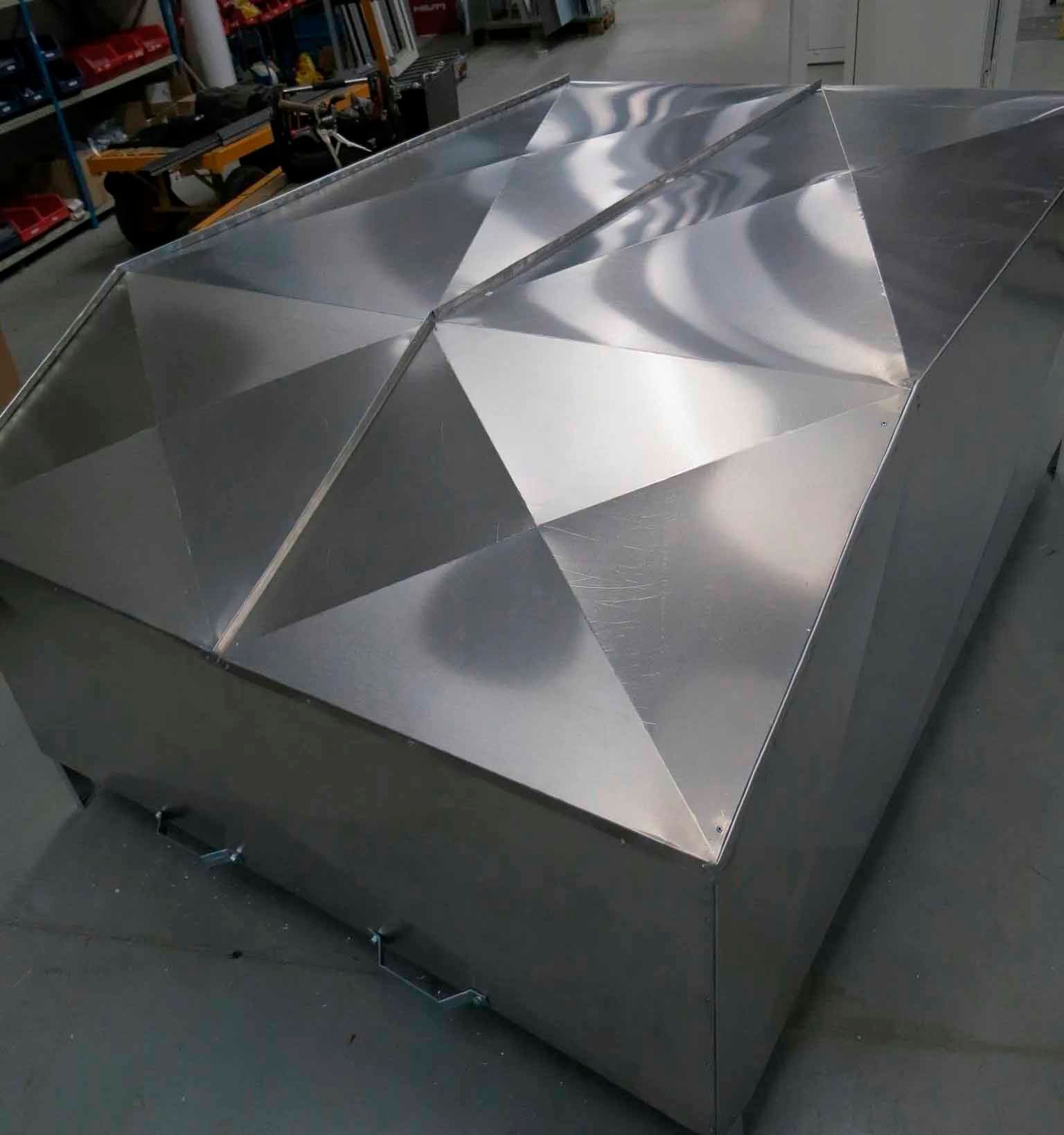 Shiny, metal box with a geometric, faceted top in a workshop setting.