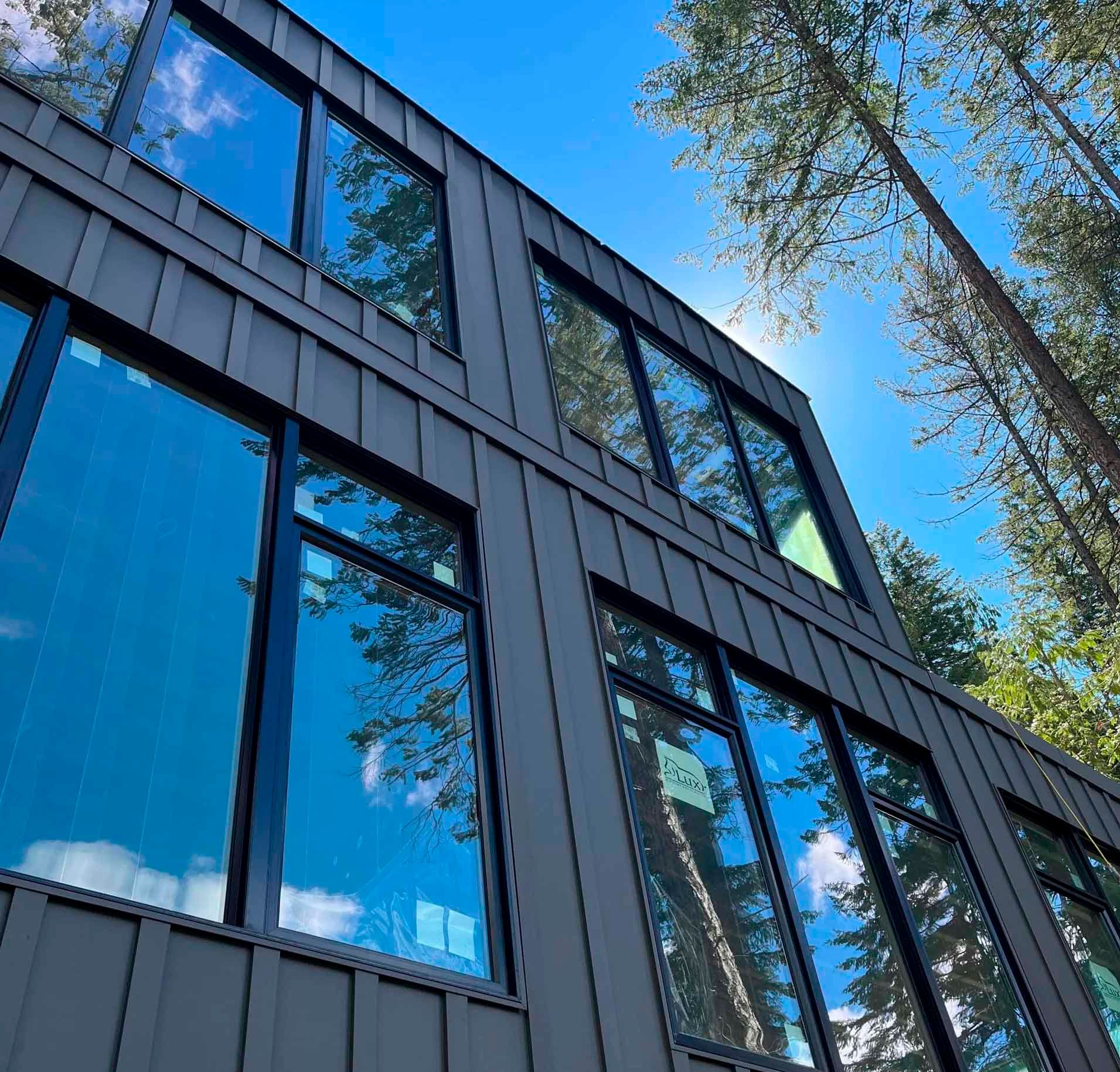Modern gray building with large windows reflecting blue sky and trees.