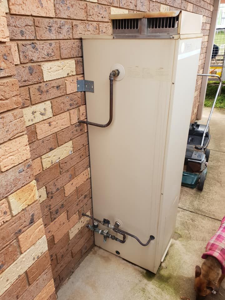 A White Water Heater is Sitting Next to a Brick Wall — Beaumont Plumbing in Glenfield Park, NSW