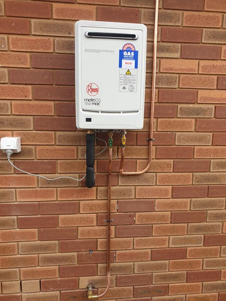 A White Water Heater is Attached to a Brick Wall — Beaumont Plumbing in Glenfield Park, NSW
