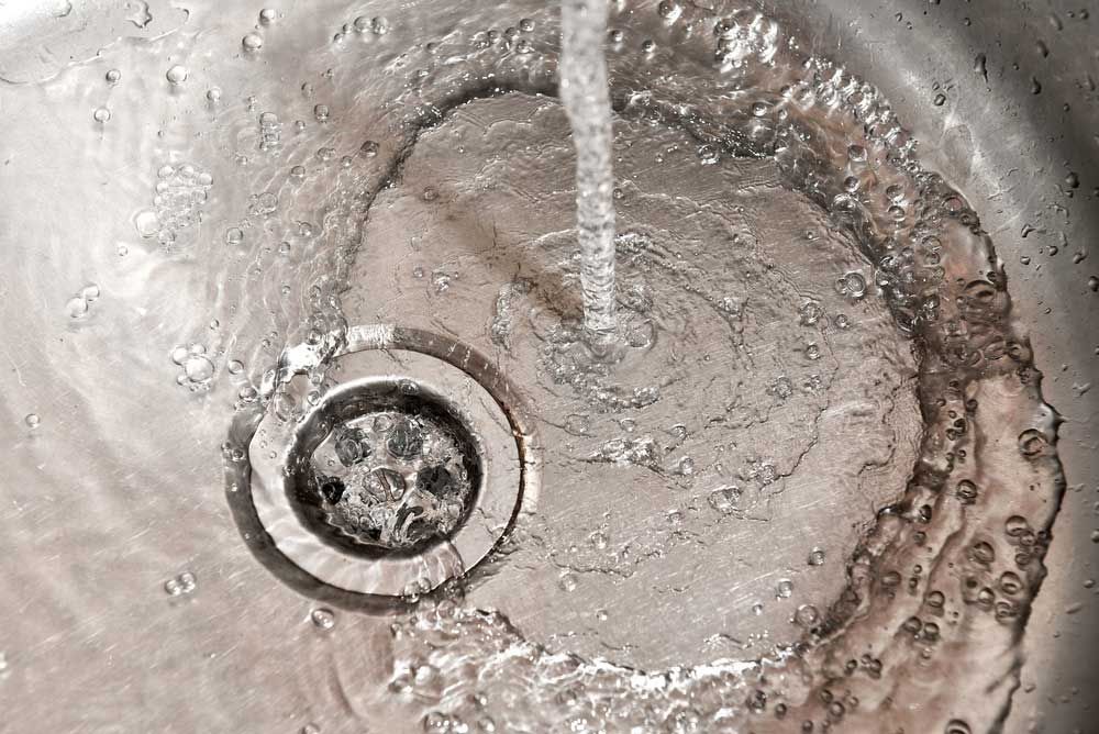 A Close Up of a Sink With Water Running Down the Drain — Beaumont Plumbing in Glenfield Park, NSW