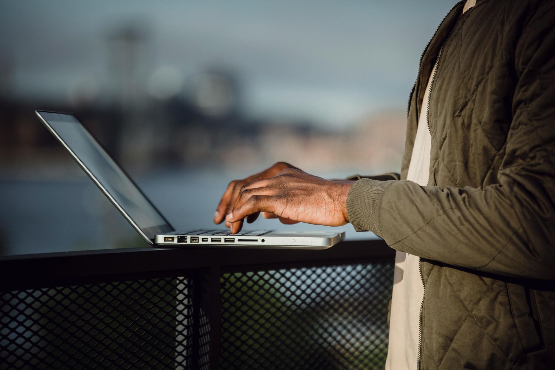 Um homem está digitando em um laptop em uma sacada.