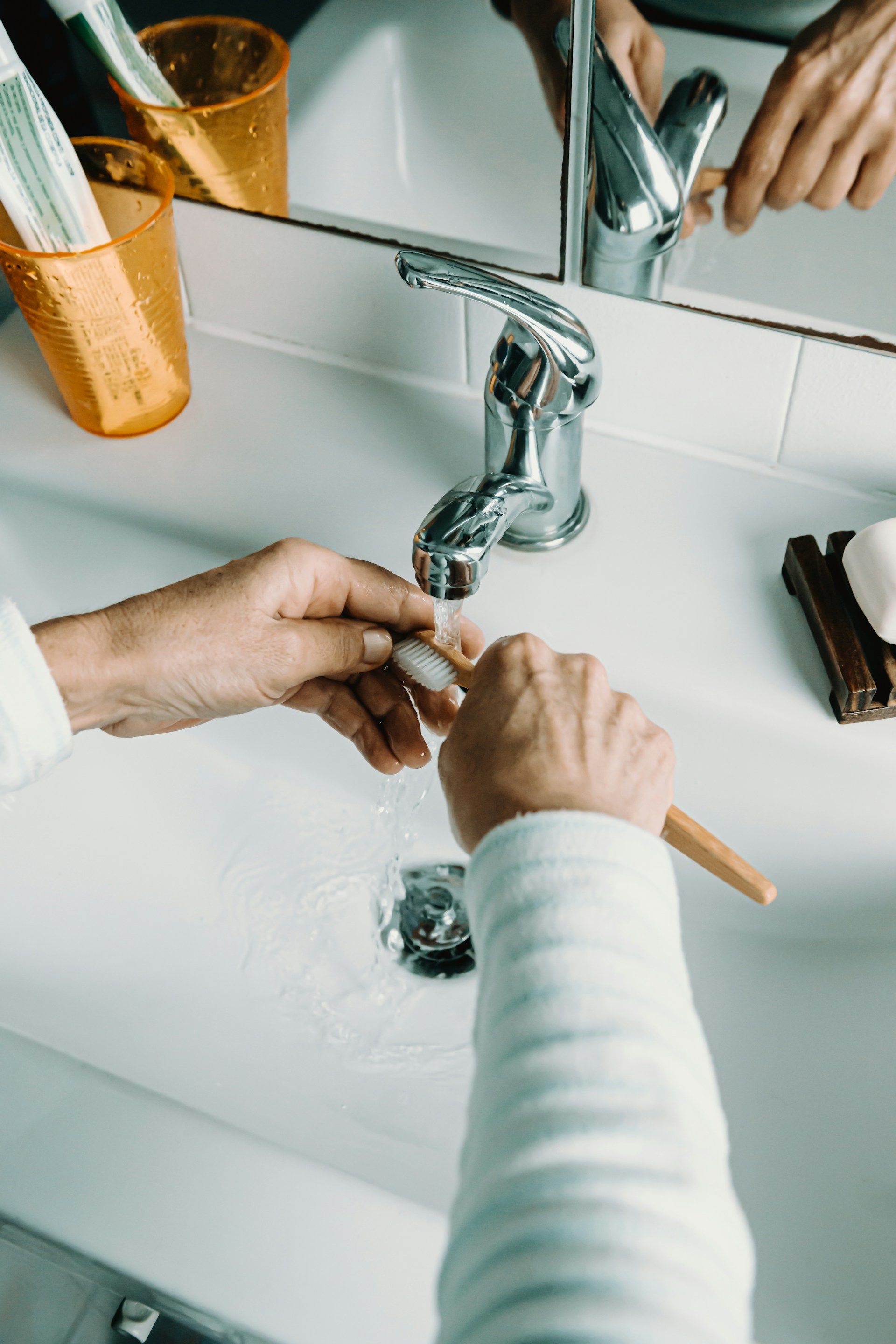 Person rinsing a makeup brush under running water in a bathroom sink.