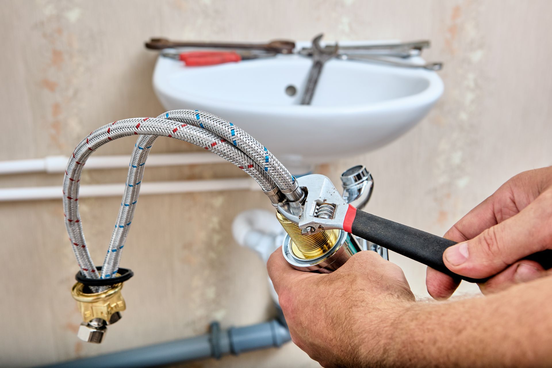 A person's hands tightening a flexible water supply line to a faucet with a wrench near a sink.