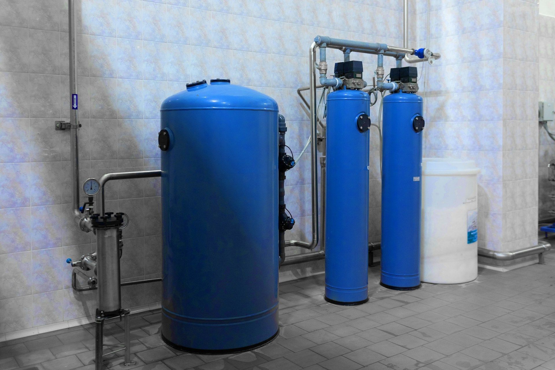 Blue water filtration system in a tiled room, with large tanks and pipes.
