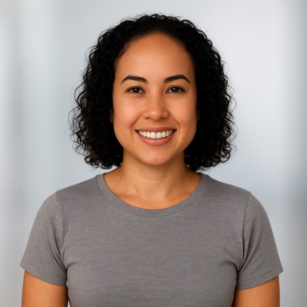 Woman with curly dark hair smiling, wearing a gray t-shirt, against a light gray background.