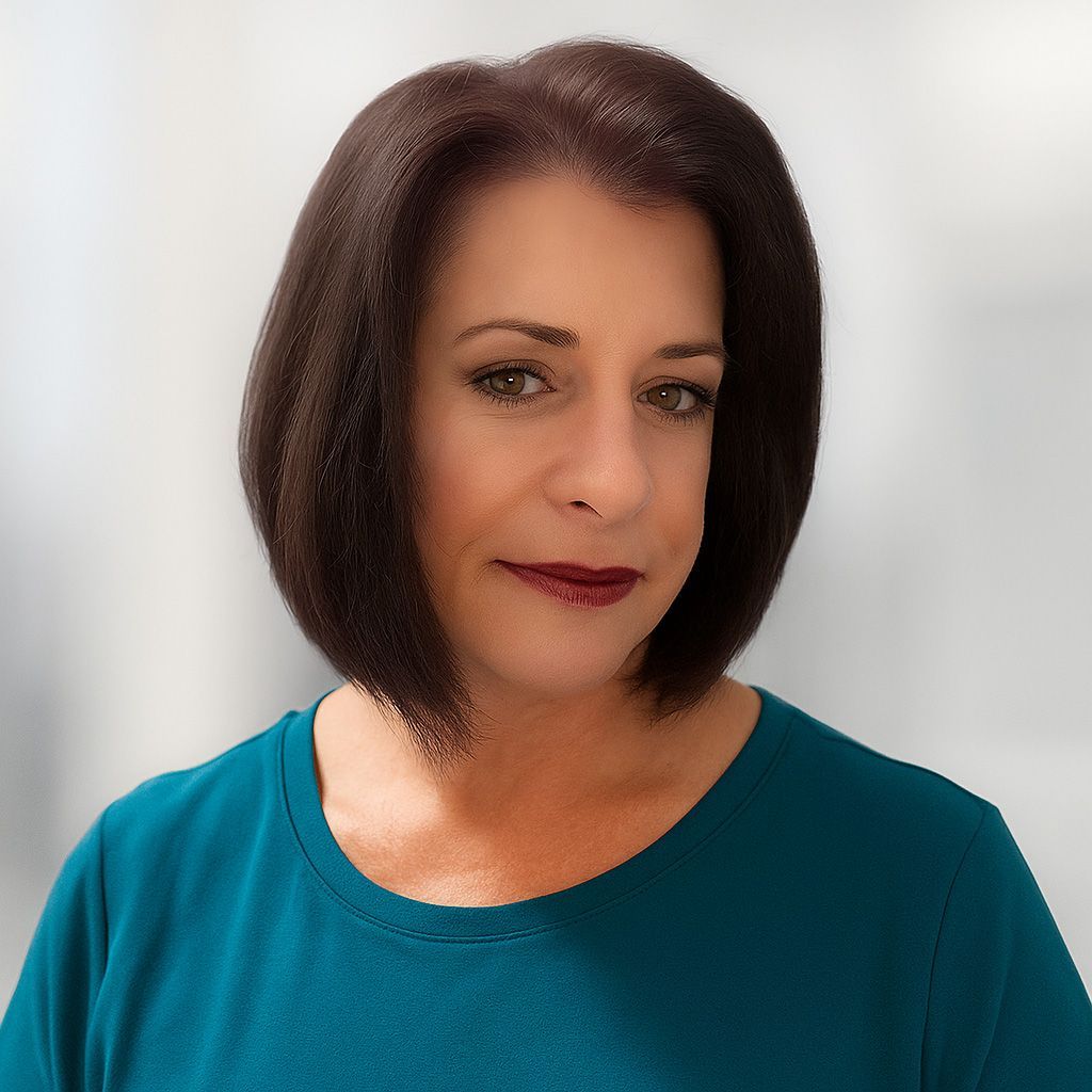Woman with dark hair and teal top smiles. Background is blurred.