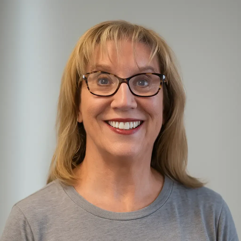 Woman with glasses smiles; light blonde hair, gray shirt, neutral background.