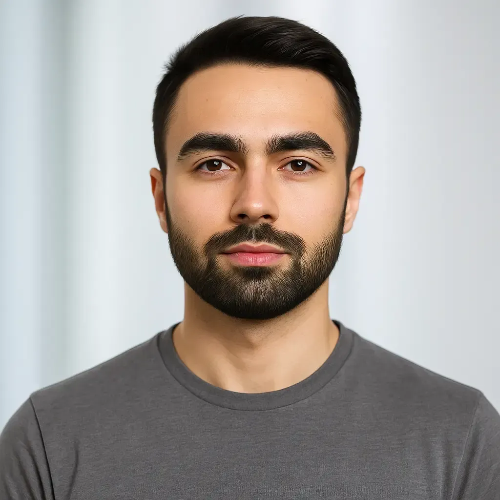 Man with dark hair and beard, wearing a gray t-shirt, looking directly at the viewer with a neutral expression.