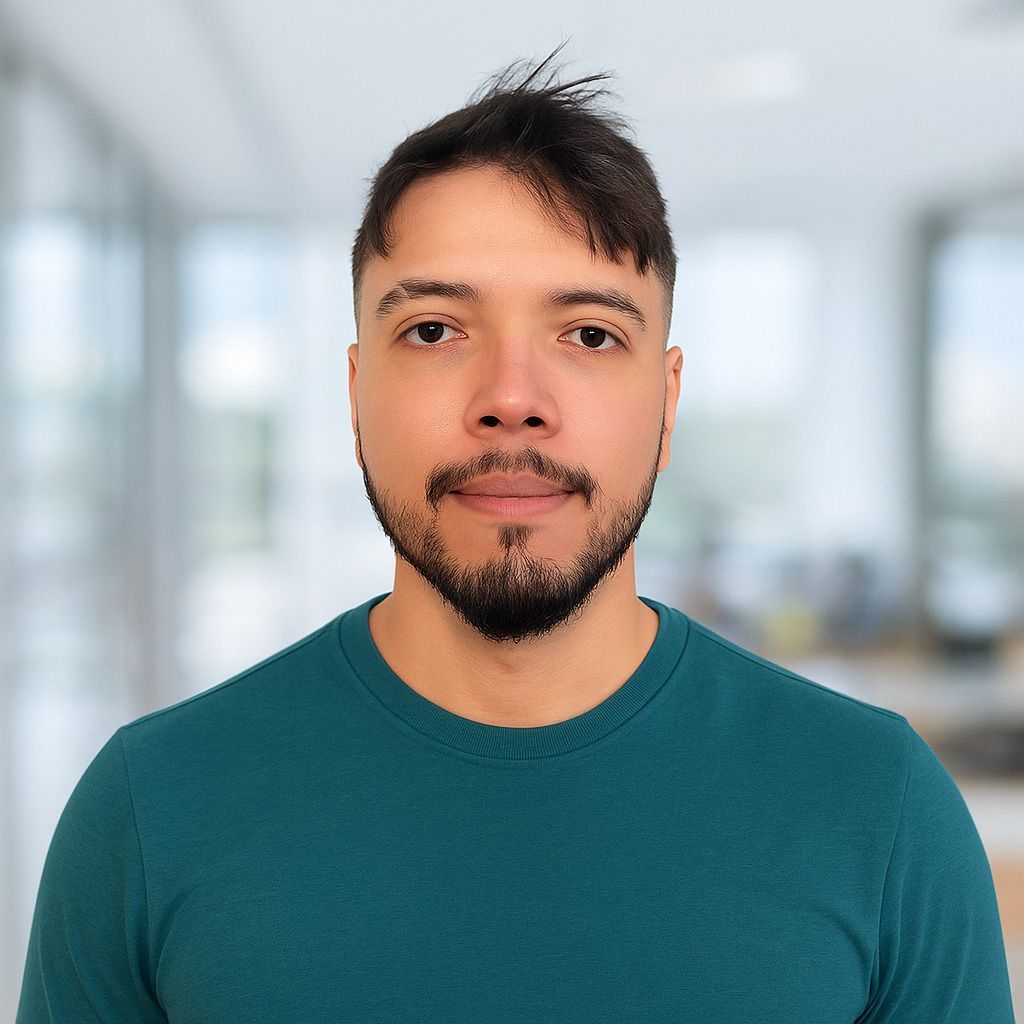 Man with a beard in a teal shirt, looking at the camera, blurred office background.