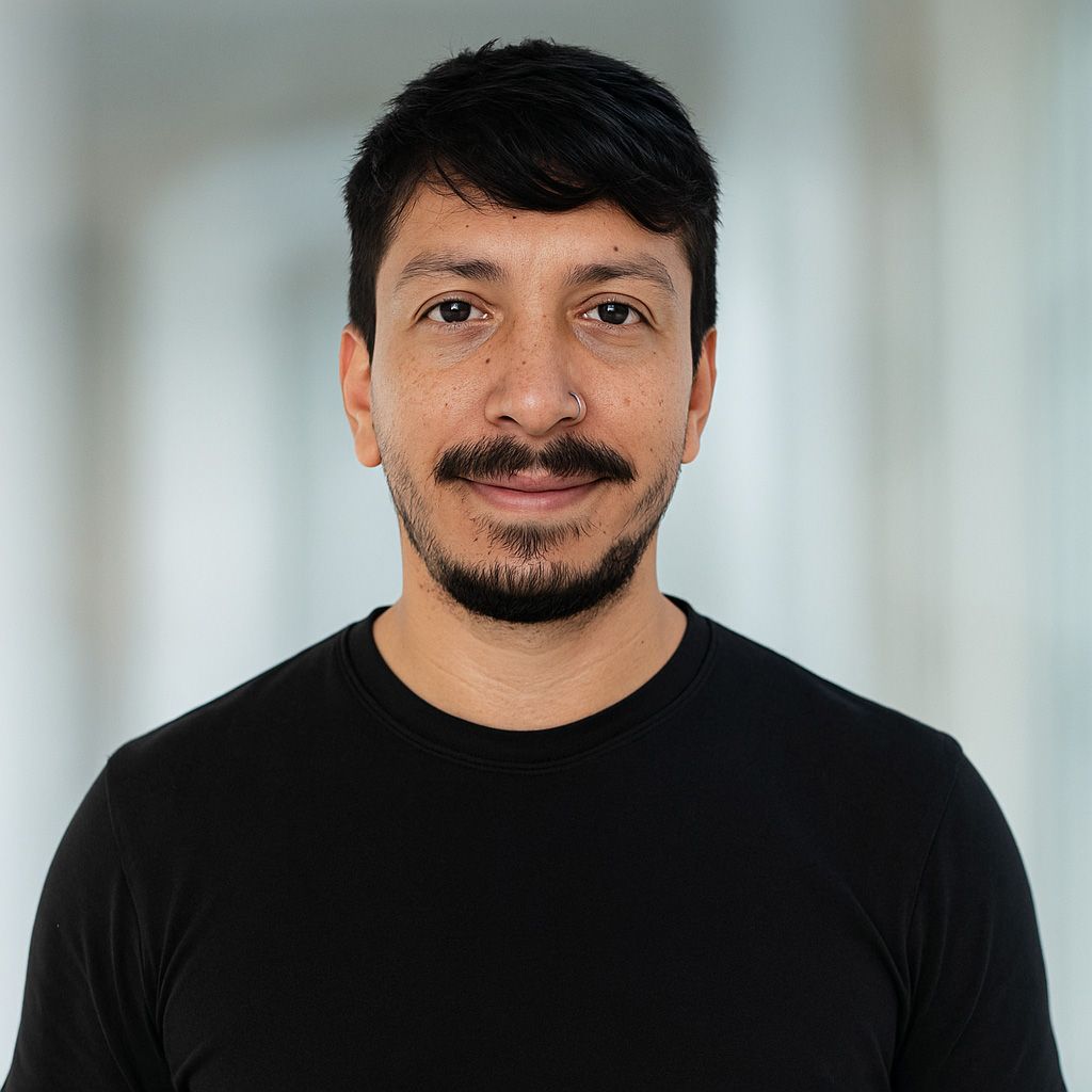 Man with dark hair, mustache, and goatee, wearing a black shirt, smiling slightly indoors.
