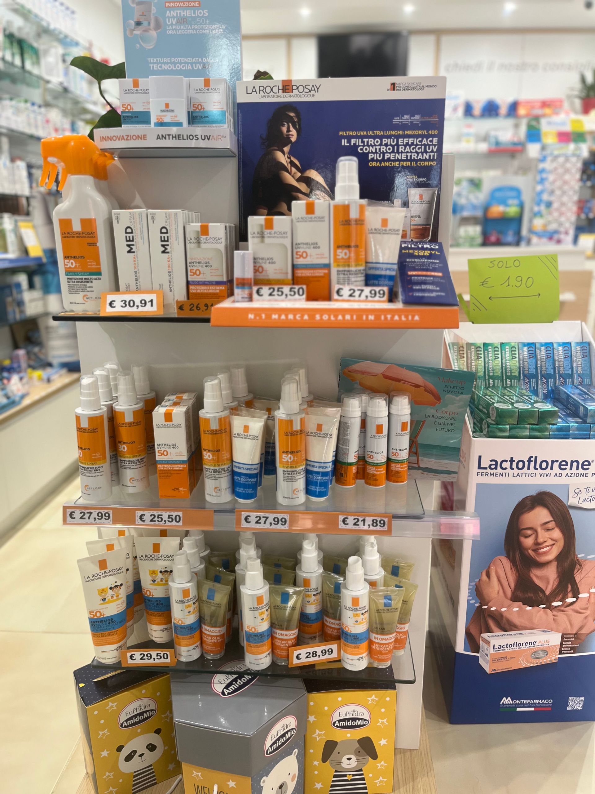 Un'esposizione di cosmetici in una farmacia con una donna sullo sfondo.