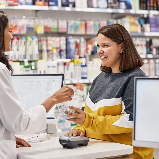 Una donna è seduta al bancone di una farmacia e parla con un farmacista.