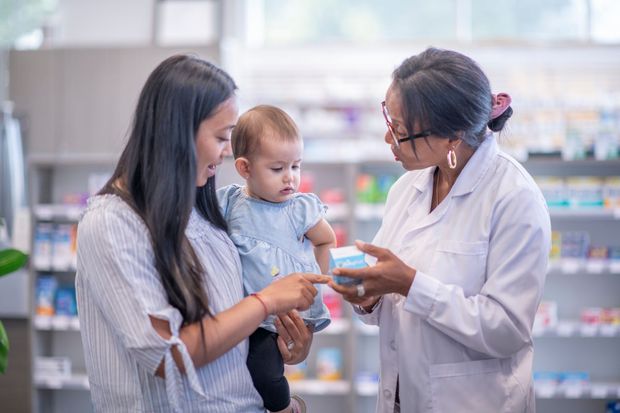 Una donna tiene in braccio un bambino e parla con un farmacista in una farmacia.