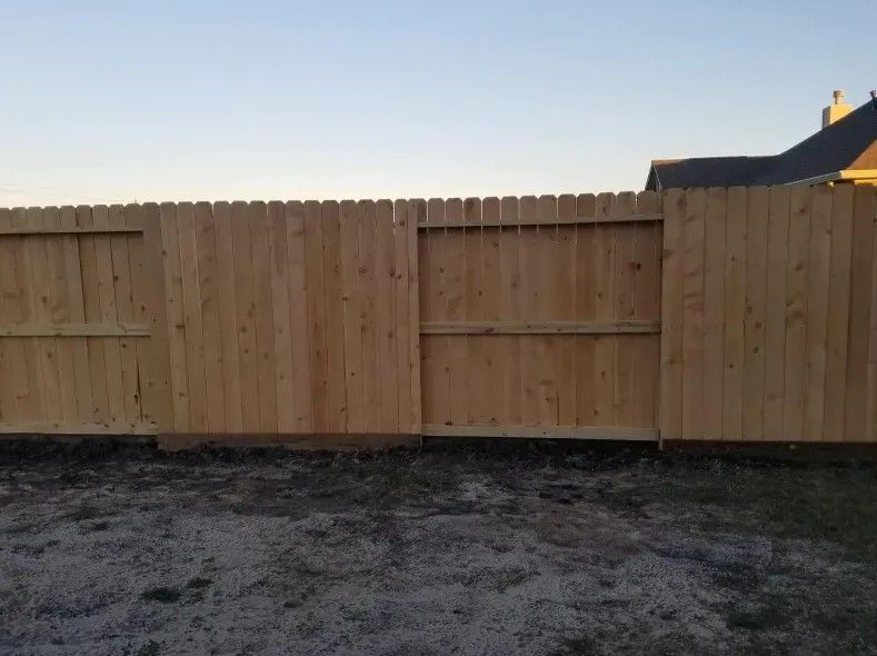 A wooden fence is sitting in the dirt in front of a house.