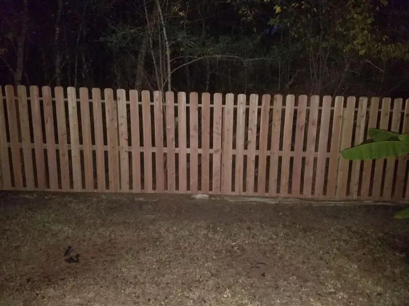 A wooden picket fence is sitting in the middle of a yard at night.