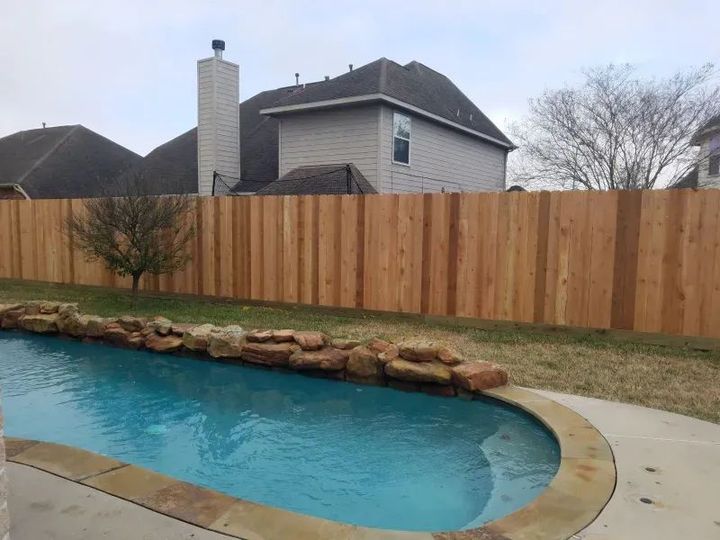 A wooden fence surrounds a swimming pool in a backyard.
