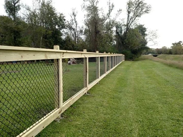 A wooden chain link fence surrounds a lush green field
