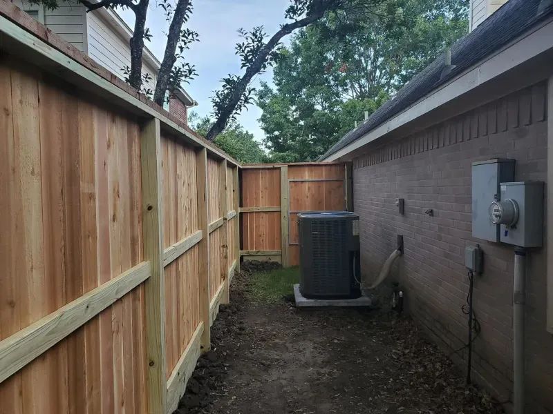 A wooden fence along the side of a house with an air conditioner in the backyard.