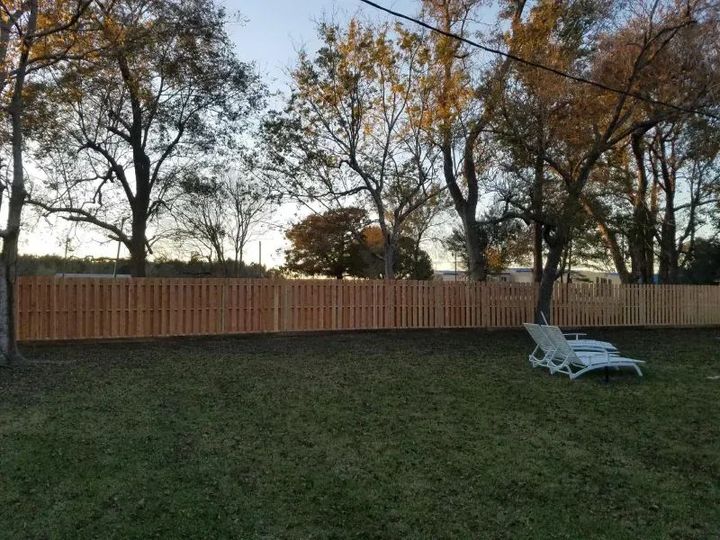 A wooden fence surrounds a lush green yard with trees in the background.