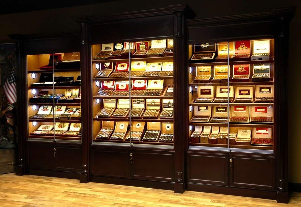 Dark wooden display cases filled with cigars and boxes, lit with interior lights, in a shop setting.