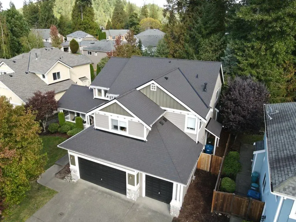Aerial view of a gray two-story house with a dark roof and a two-car garage, surrounded by trees.