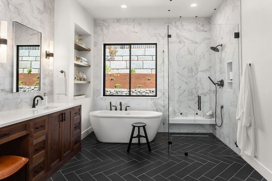 Modern bathroom with marble shower, soaking tub, dark wood vanity, and black herringbone tile floor.