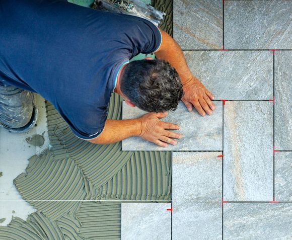 Person installing gray tiles on a floor, using tile spacers.