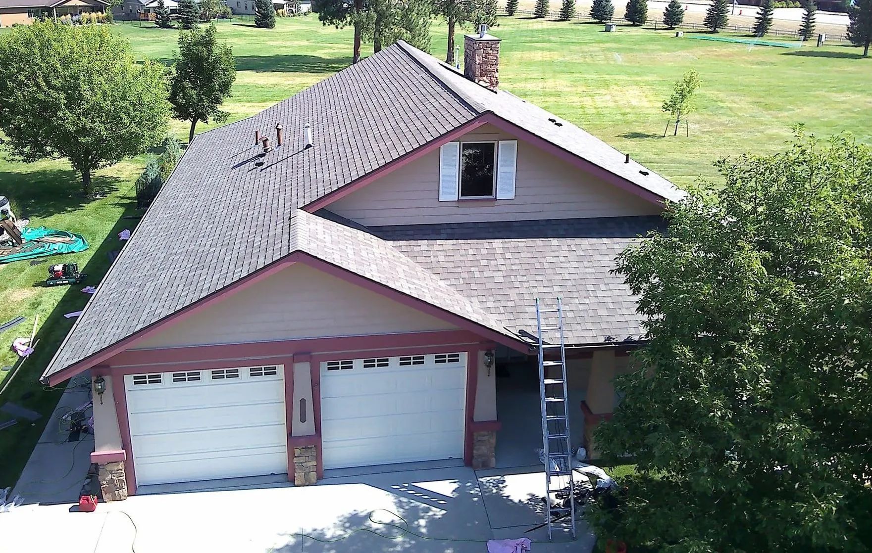 An aerial view of a two-story house with a garage, ladder, and a partially replaced roof. Green
tre