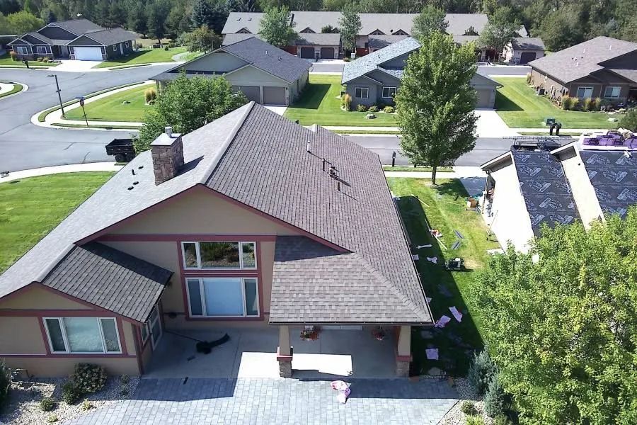 Aerial view of residential homes with green lawns and trees. Brown roofed house in foreground.