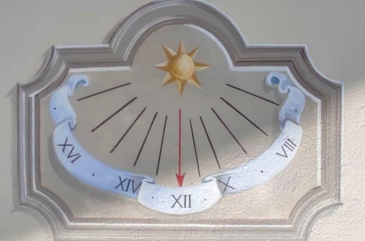 Un orologio su un muro con numeri romani e un sole