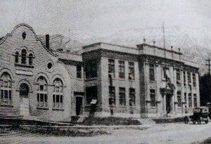 A black and white photo of a building with a horse drawn carriage parked in front of it.