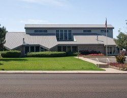 A large building with a gray roof and a large lawn in front of it.