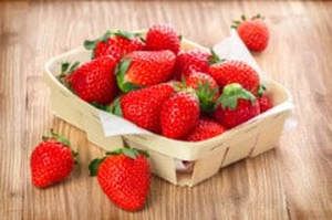 A wooden basket filled with strawberries on a wooden table.