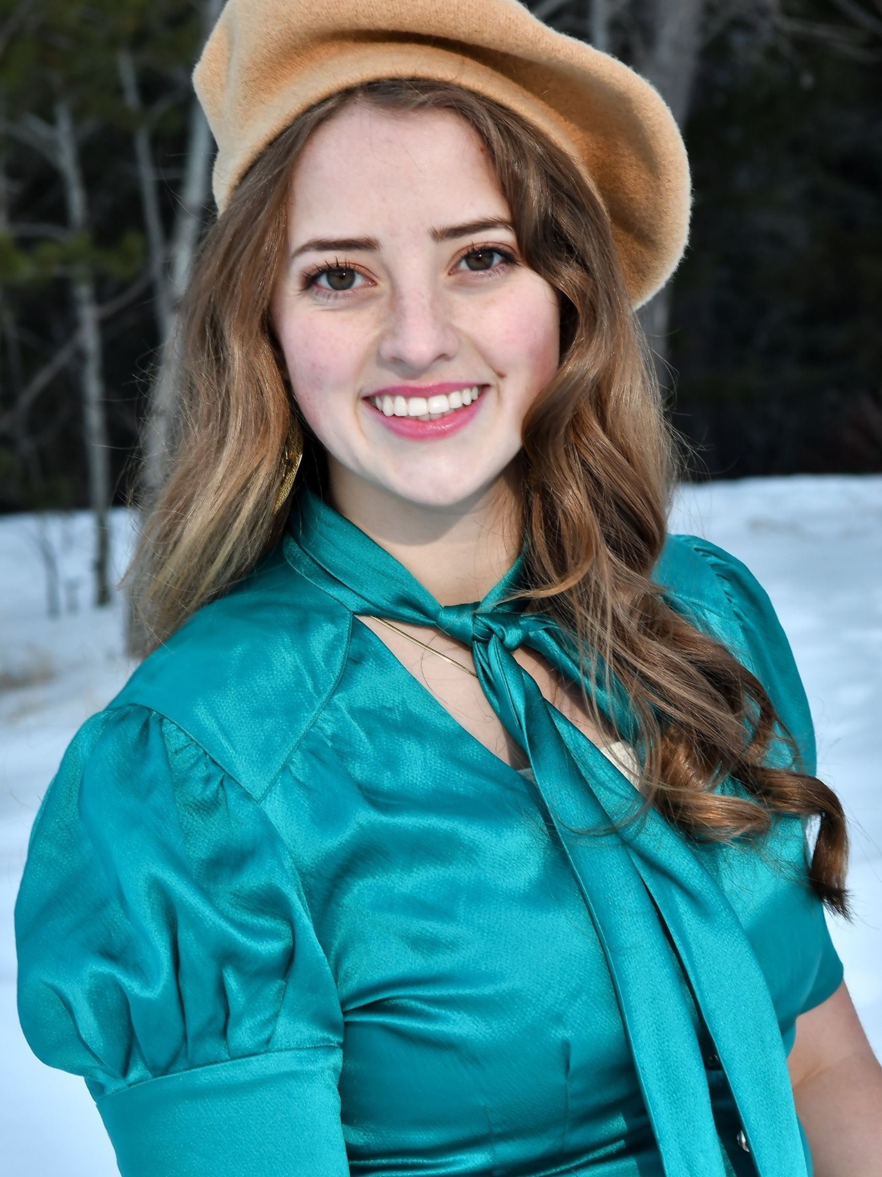A woman in a white dress is leaning against a wooden wall and smiling.