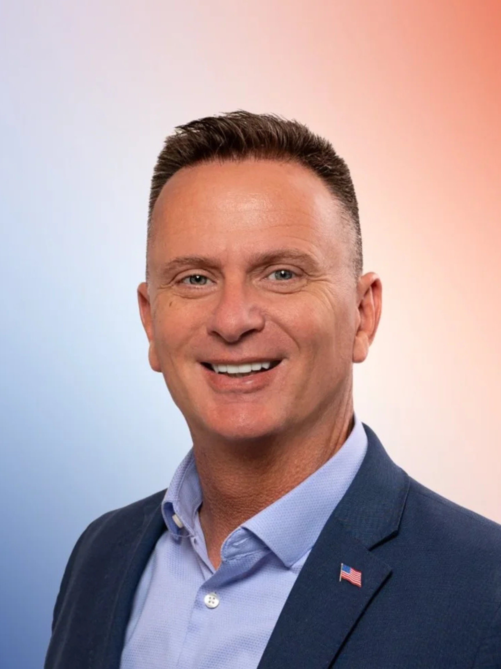 A man in a suit and tie is standing in front of a white brick wall with his arms crossed.