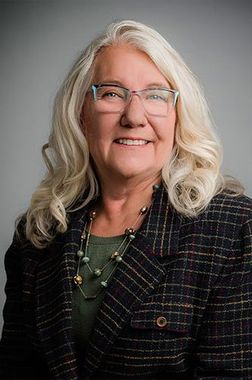 A woman wearing glasses and a plaid jacket is smiling for the camera.