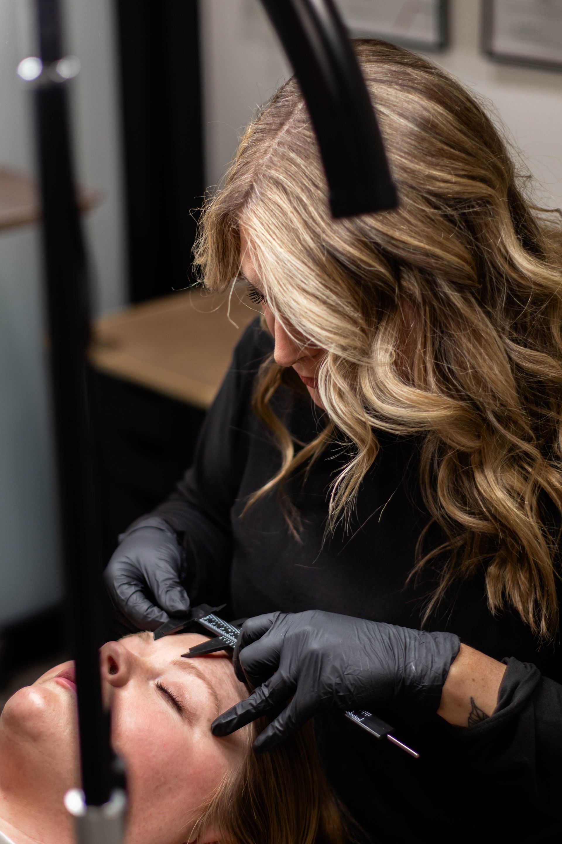 A woman is applying makeup to another woman 's eyebrows.