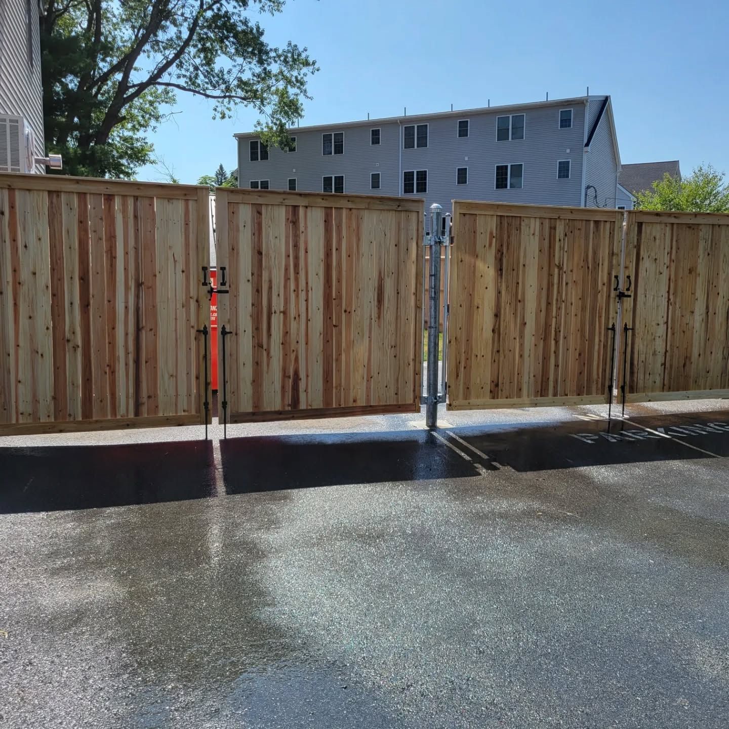 Wooden fence with a gate, in a paved area, under a bright blue sky.