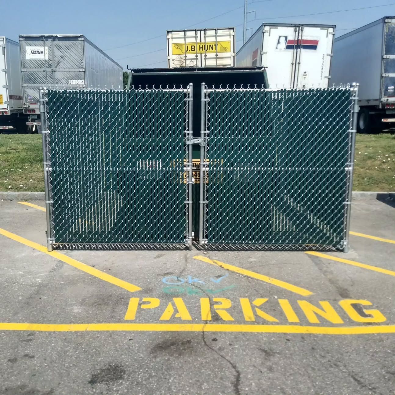 Green chain-link fence gate, partially blocking parking spot marked 