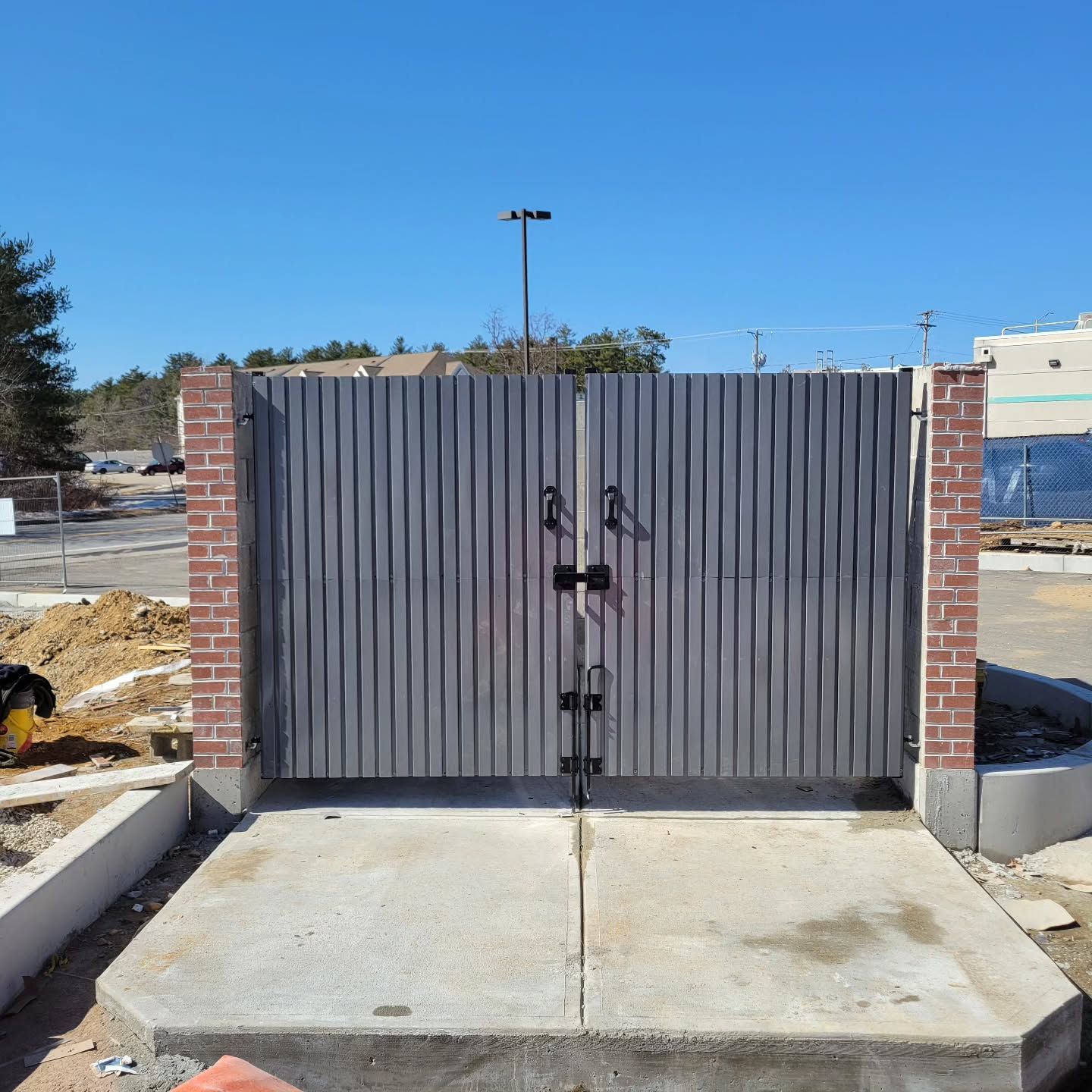 Gray metal double gates with brick columns, concrete pad, against a blue sky.