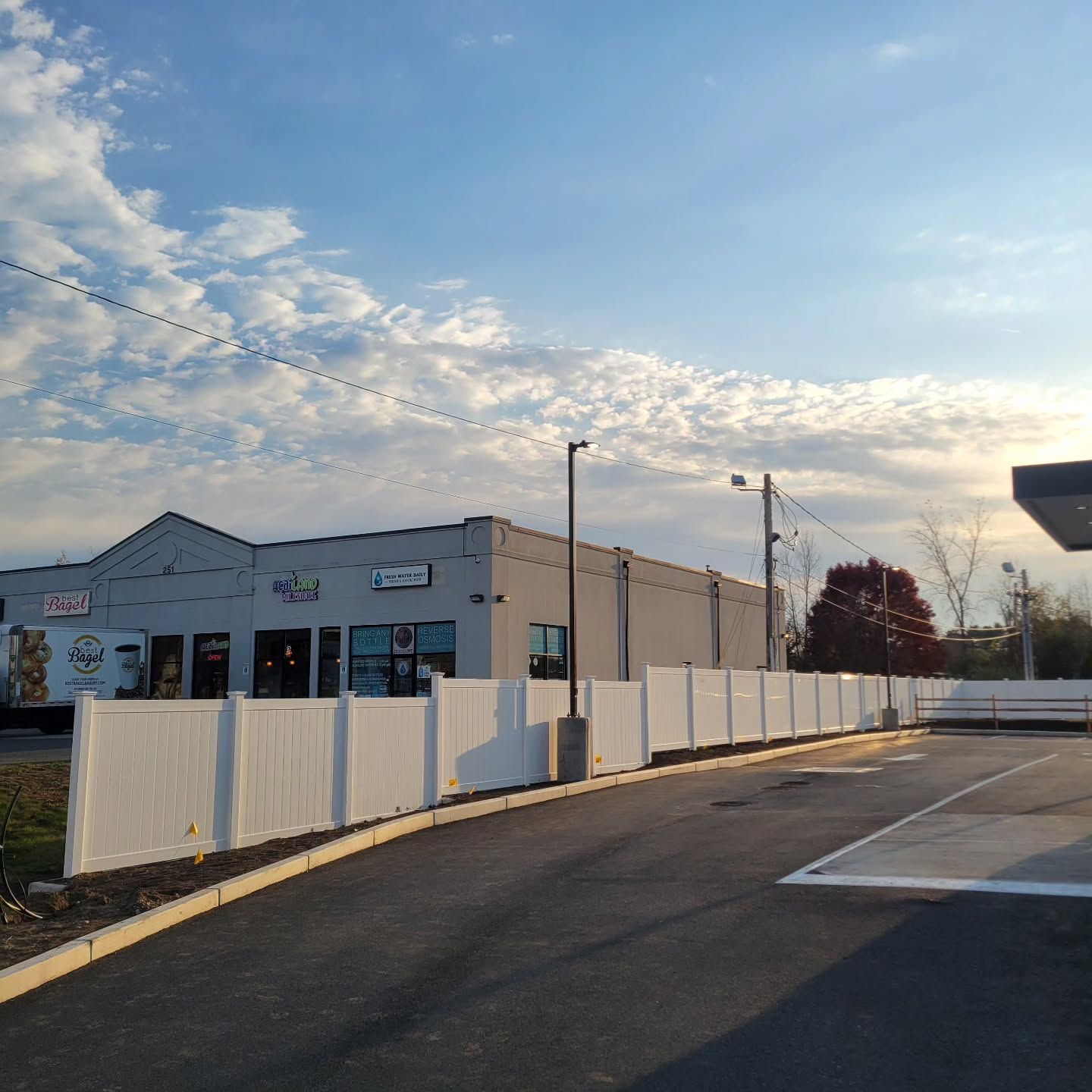 Exterior view of a commercial building behind a white fence under a partly cloudy sky.