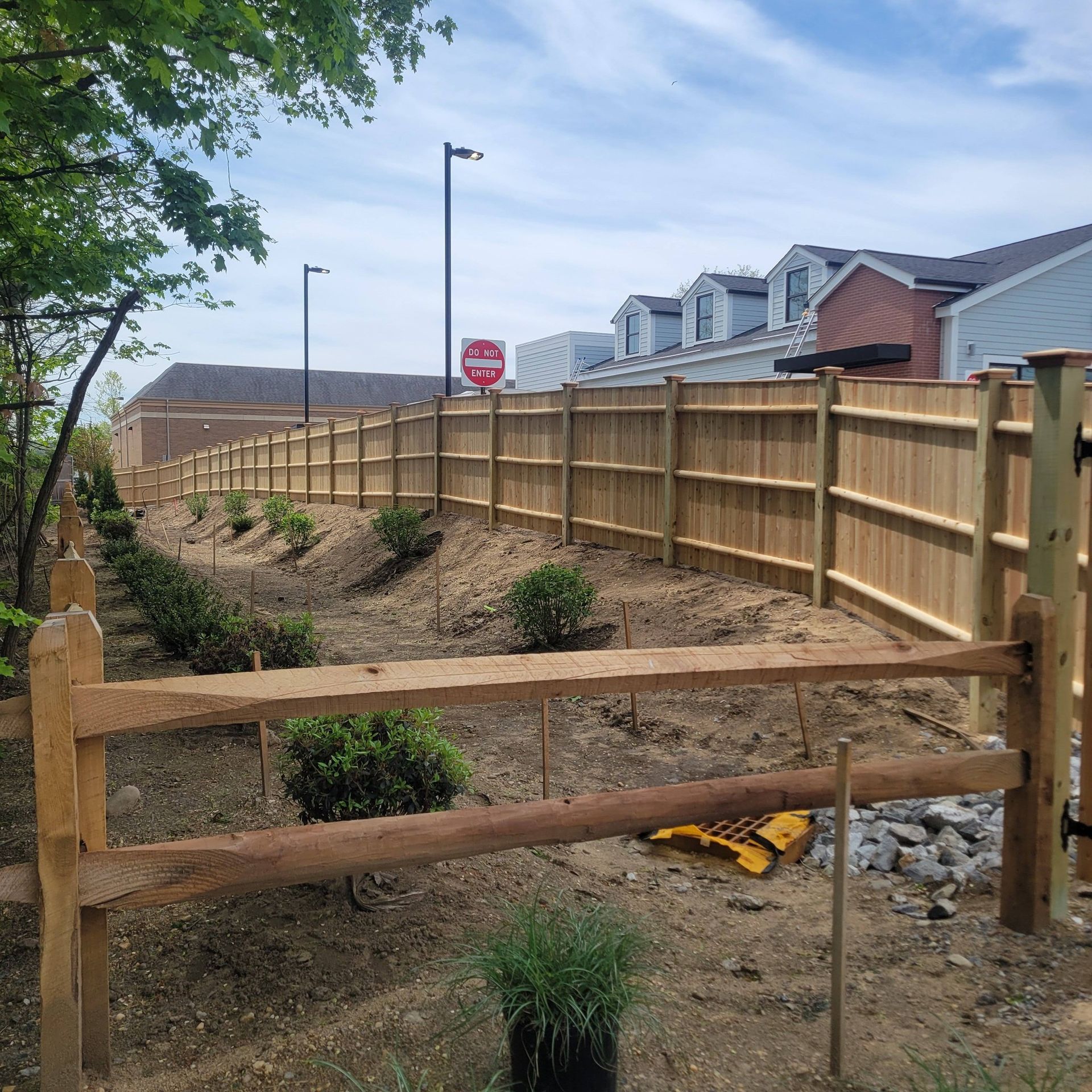 A new wooden fence surrounds a landscaped area next to a row of townhouses.