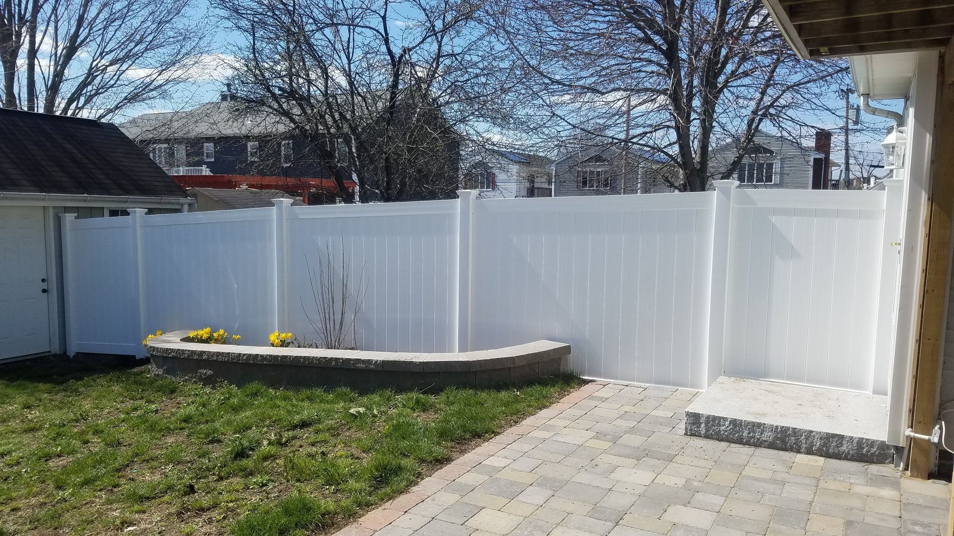 White vinyl privacy fence in a backyard, beside a patio.