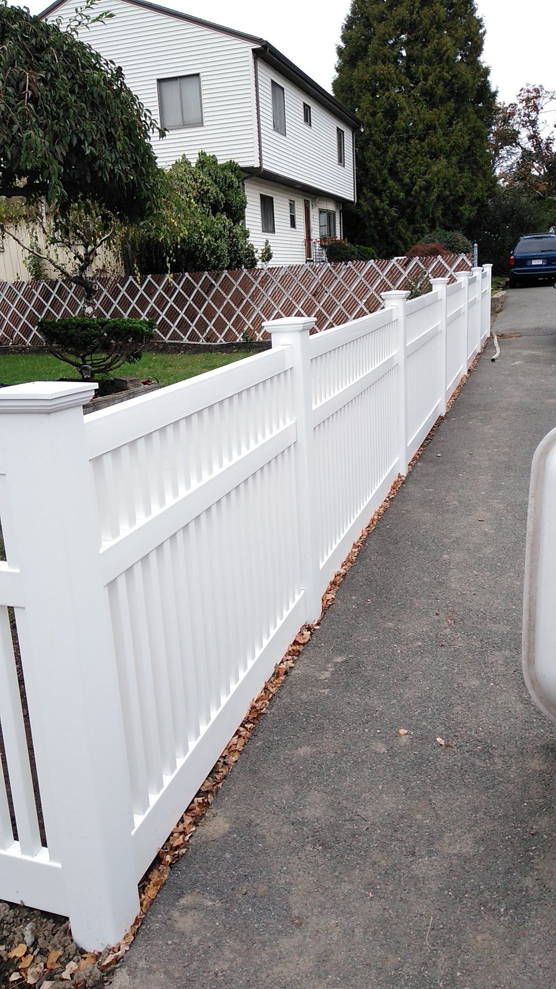 White vinyl fence along a driveway in front of a house.