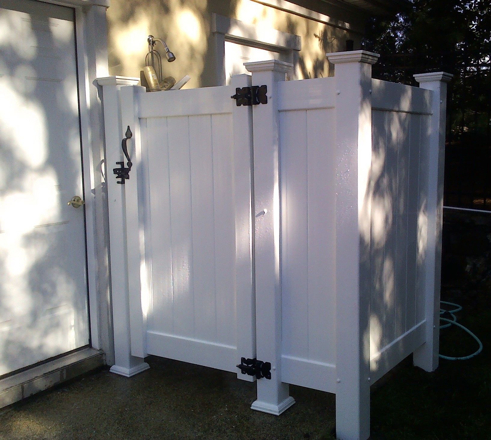 White outdoor shower enclosure next to a white door. Black hardware, sunlight.
