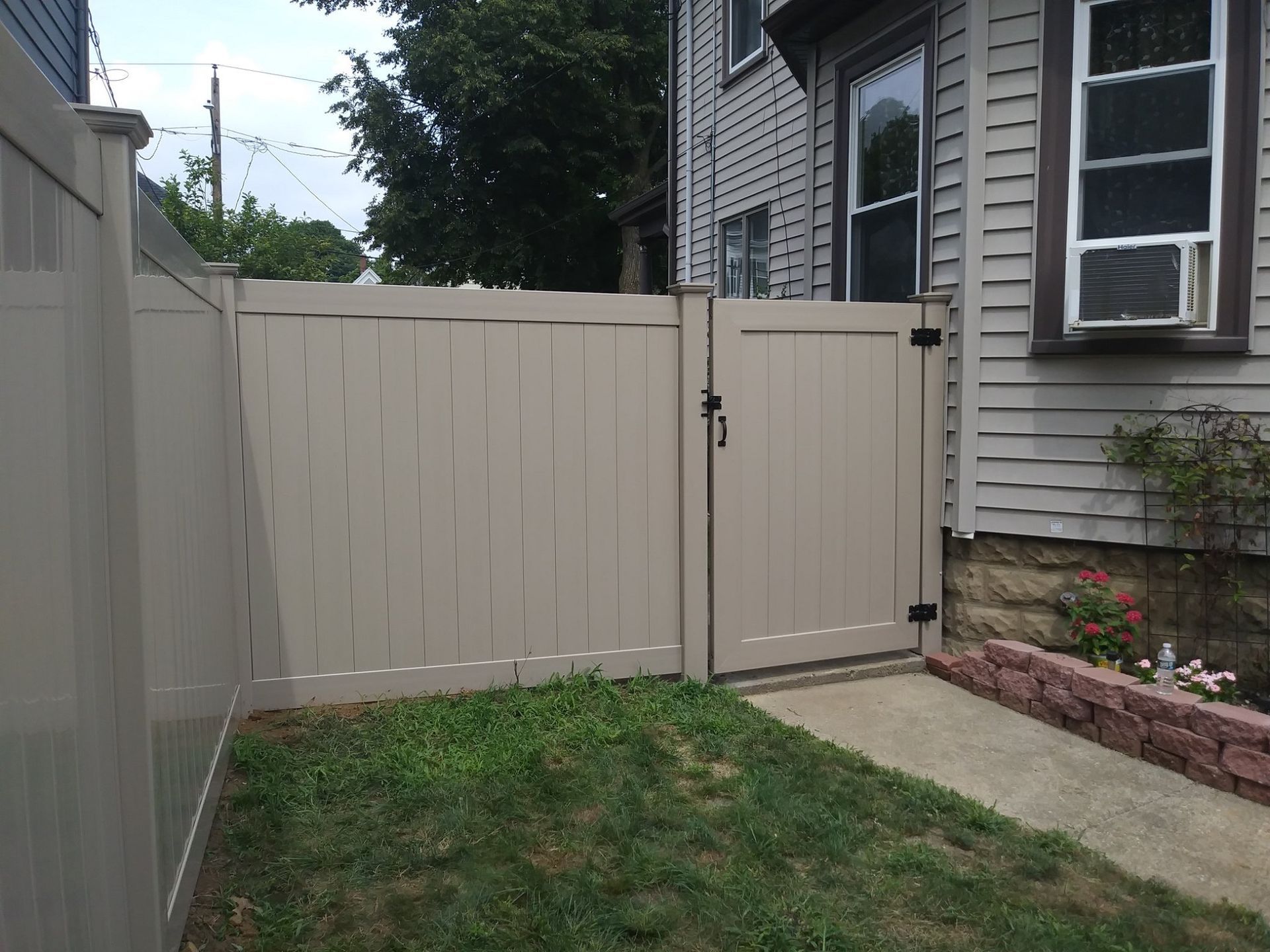 Tan vinyl fence with matching gate next to a house with a window and AC unit.