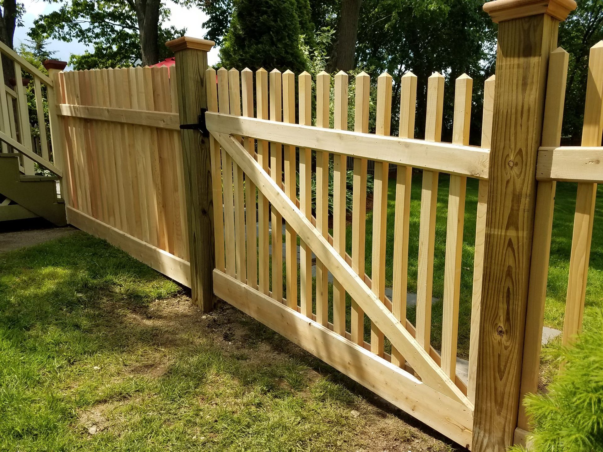 Wooden fence with gate in a yard, with vertical pickets and horizontal planks.
